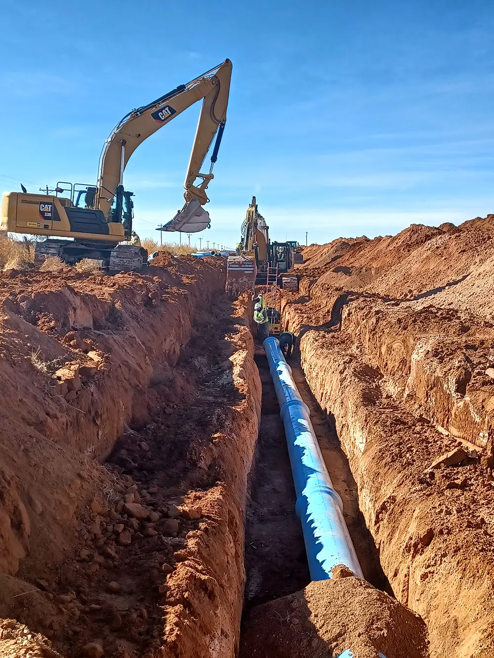 CAT vehicles next to large trench with a blue pipeline